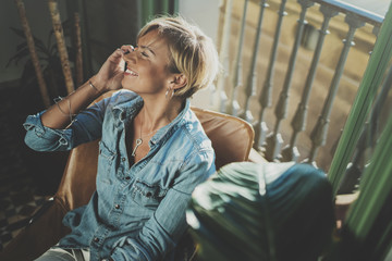 Fototapeta premium Smiling young woman wearing casual clothes and talking on smartphone device while spending relax time in vacation travel.Attractive woman owner communicating on cellular.Blurred background.