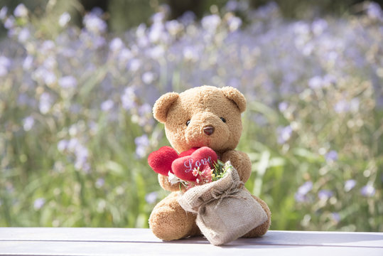 Brown bear and red heart with blurred floral floor.