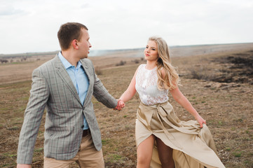 Fototapeta na wymiar Handsome guy and blonde girl walking on the field, a man leads a woman holding the hand