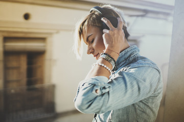Fototapeta premium Smiling beautiful girl relaxing at home,wearing casual clothes,playing music,using smartphone and listening audio books in modern headphones.Young pretty woman music lover at room.Blurred background.