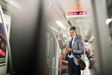 Mature businessman with smartphone in a metro train.