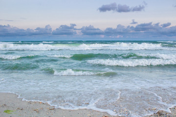 Sea coastal waves rolling on sandy beach, cloudy sunrise