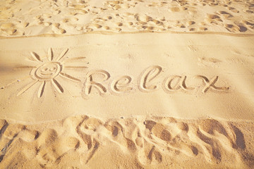 Drawing  picture of the sun, traces and word relax on golden sand on sunny sandy beach. The concept of beach recreation, summer vacation rest, pattern, texture of sand.