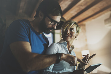 Happy family couple using electronic tablet in livingroom at home.Bearded man in eye glasses making conversation with young blonde woman at night. Blurred background.