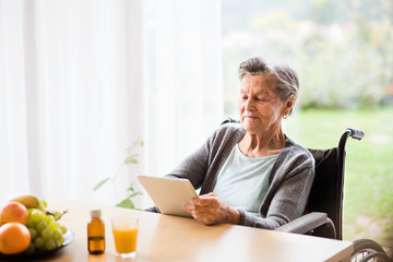 Senior woman in a wheelchair with tablet at home.