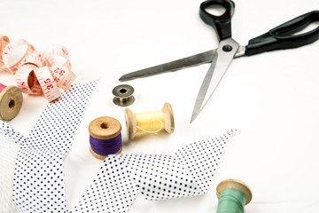 Set of tools and accessories for sewing and needlework with threads in spools, needles, measuring tape and other items on a white background