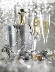 Two glasses of champagne with bottle in cooler on a silver bokeh background