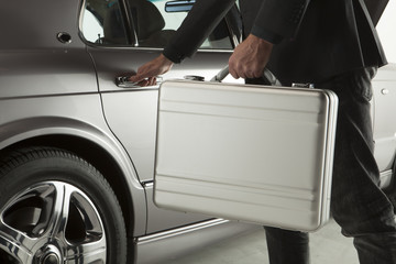 Close-up of man in formalwear opening a car door with a briefcase
