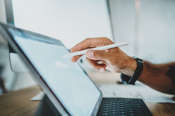 Close up view of male hand drawing at portable tablet computer at wooden table desk in modern lightful office.Horizontal.Blurred background.Cropped.
