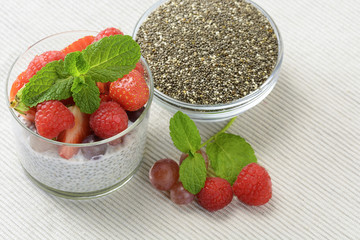 Healthy coconut milk chia pudding in a glass with fresh berries, leaves mint and chia seeds in glass bowl