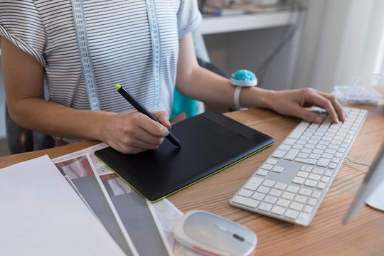 Mid section of female designer using graphic tablet at desk