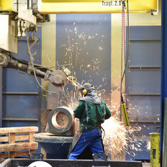 Arbeiter in einer Giesserei verputzt Werkstücke mit einer Schleifmaschine // Worker in a foundry...
