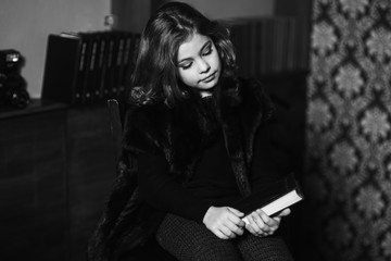 Beautiful little girl is reading a book in the library.