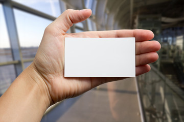 Hands holding a white business visit id card, gift, ticket, pass, present showing close up on blurred blue background. Copy space for ad text