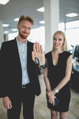 Beautiful couple in vehicle showroom holding keys from new car. Man and woman choosing new electro car. Image with selective focus.