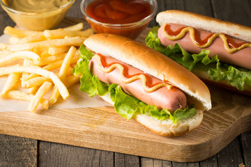 Tasty barbecue grilled hot dog with salad,yellow mustard, onion, ketchup, and French fries on wooden background. Junk and fast food concept.