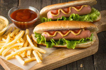 Tasty barbecue grilled hot dog with salad,yellow mustard, onion, ketchup, and French fries on wooden background. Junk and fast food concept.