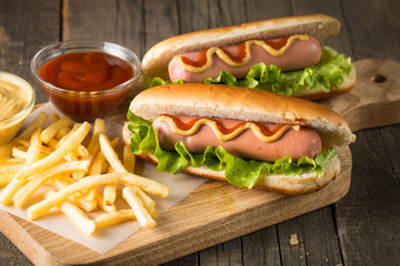 Tasty barbecue grilled hot dog with salad,yellow mustard, onion, ketchup, and French fries on wooden background. Junk and fast food concept.