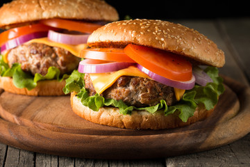 Close-up photo of home made hamburger with beer made of beef, onion, tomato, lettuce, cheese and spices. Fresh burger closeup on wooden rustic table with potato fries and chips.