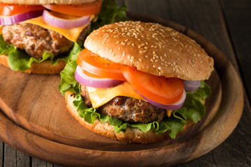 Close-up photo of home made hamburger with beer made of beef, onion, tomato, lettuce, cheese and spices. Fresh burger closeup on wooden rustic table with potato fries and chips.