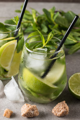 Fresh made mojito cocktail with lime, brown sugar, ice cubes and mint on a grey stone background. Alcoholic drink and lemonade concept.