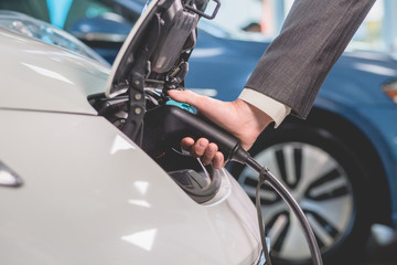 Close up view of man recharging electric car. Mans hand plugging out power cord to electric car.