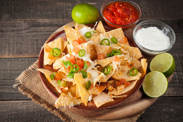 Corn Mexican nachos with beef, jalapeno, cheese, pepper, olives and chili con carne on a wooden background. Lime, Ketchup, sour cream and mayonnaise souce seasoning.