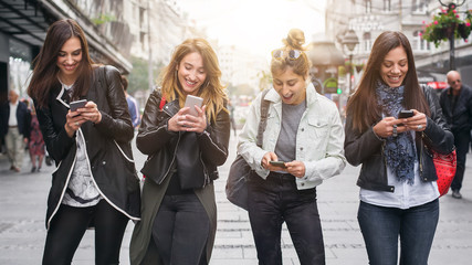 Happy four friends walking on the street and using cellphones