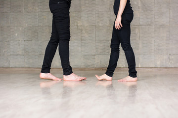 Education of modern dance. Young boy and girl in black clothing standing with bare feet on grey background. School of modern dance.