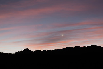 The crescent moon and a few stars linger in the sky among pink and orange clouds before sunrise on the Wire Mesa trail in Southern Utah