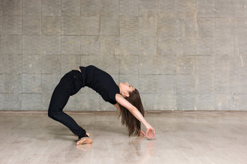 Female dancer practicing gymnastic element. Young woman dancer posing on studio background. Dance art studio.