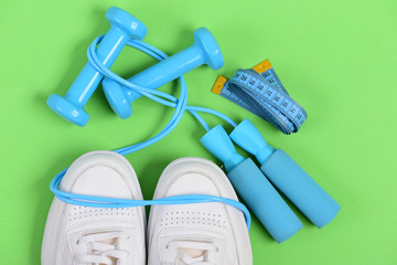 Sneakers with skipping rope and tape on green background.