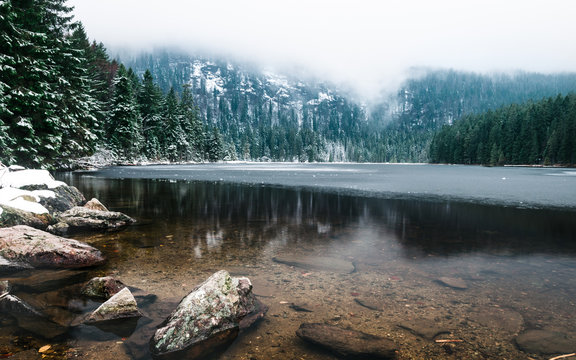 Arbersee gefroren mit Spiegelung und Schnee und Eis und Nebel mit Bergen im Hintergrund im Bayerischen Wald