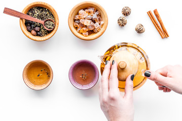 Tea ceremony concept. Hand takes tea pot near cups and dry tea leaves on white background top view