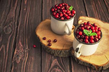 Fresh red cranberries with mint leaves in a white cup on a dark wooden background. Berry background, healthy food, red berry.