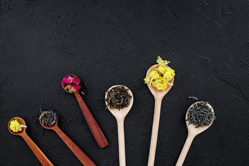Aromatic tea. Wooden spoons with dried tea leaves, flowers and spices on black background top view copyspace