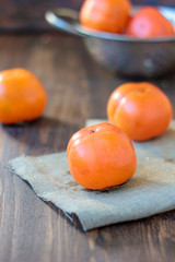 Group of persimmons on wooden table and piece of fabric.