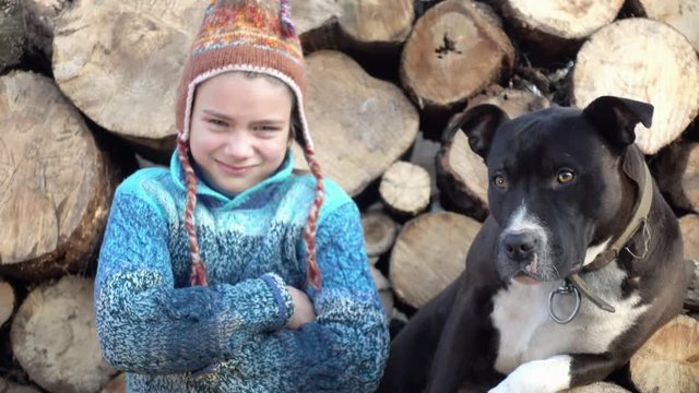 Staffordshire terrier licks a sad boy, against the background of firewood. Portrait of a child in the background of firewood with a dog 4K video.
