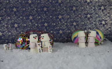 Christmas photography image of marshmallows shaped as snowman with tree decoration baubles on star pattern background and snow base