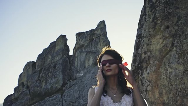 Closed eyes in a beautiful girl in a white dress against the background of the sunset against the background of rocks.
