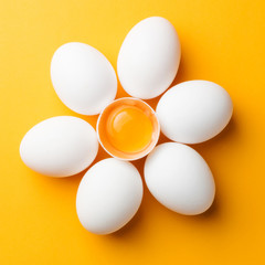 White eggs and egg yolk on the yellow background. topview, square