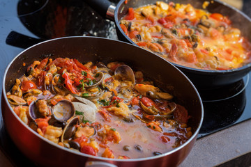 Close-up of frying pans with seafood dish cooked in tomato sauce. Fresh stewed Clams, Shrimps, mussels and squid, base for Italian pasta