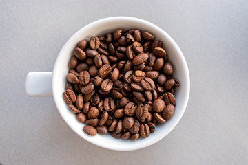 White cup with coffee beans on gray woden background