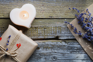 Top view of the gift in a kraft paper, the bouquet with lavender and the burning candle in shape of heart on the old wooden background. Copy space.