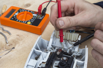 Elektryk naprawia zepsute żelazko i mierzy miernikiem przepływ prądu. - obrazy, fototapety, plakaty