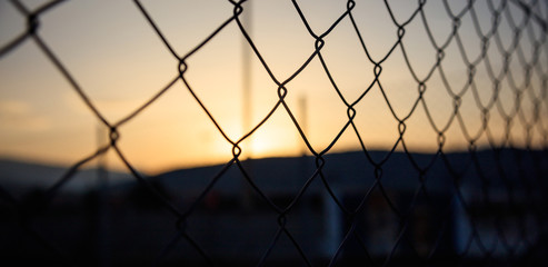 Steel wire mesh fence on a sunset background. Blurred smokestacks and hills silhouette.