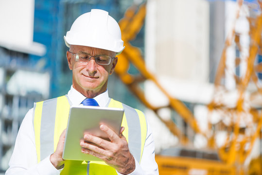 Construction manager controlling building site and tablet device in his hands