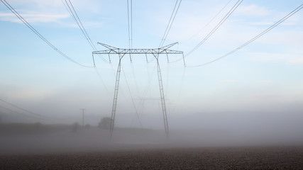 Large power lines in a foggy landscape in the sunrise.