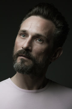Fabulous at any age. Portrait of 40-year-old man standing over dark gray background. Close up. Classic style. Scar on forehead. Model is looking up. Studio shot