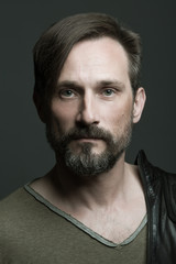 Fabulous at any age. Portrait of 40-year-old man standing over dark gray background. Close up. Rocker, biker style. Scar on forehead. Studio shot